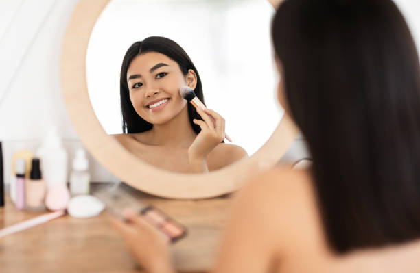 istock Attractive smiling asian woman applying blush on her face 1285255204
