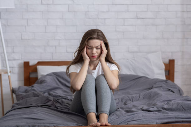 istock Unhappy millennial lady sitting on bed and massaging her temples, having headache or depression 1285255268