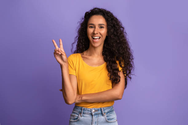 istock Joyful Young Woman Gesturing Peace, Having Fun While Posing Over Purple Background 1285256134