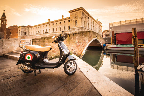 典型的なイタリアのスクーターベスパは、夕日の光の背景に橋と古代のブイディングとギオッジャヴェネツィアの運河の近くに駐車 - ベスパ ストックフォトと画像