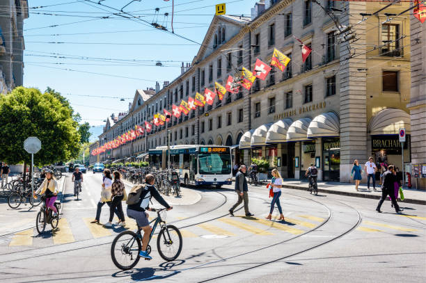 Pedestrians and cyclists crossing the street in Geneva. Geneva, Switzerland - September 4, 2020: Pedestrians and cyclists are crossing the rue de la Corraterie, with buildings decked with flags of Geneva and Switzerland, as a bus is waiting at a red light. geneva switzerland stock pictures, royalty-free photos & images