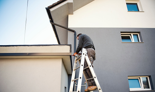 Roofer builder worker finishing folding a metal sheet, he is up a ladder,