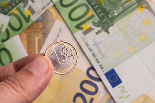 One euro coin in men's fingers against the background of several 100 and 200 euro bills