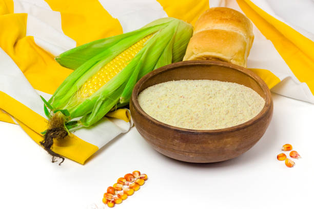 Corn flour in ceramic bowl, fresh ear of corn and cornbread on tablecloth isolated on white background. Healthy, organic food concept.