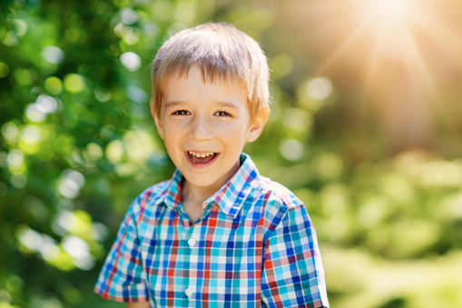 Happy child smiling outdoors on sunny day. Cute boy laughing in park