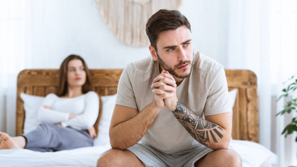 Man and woman feeling stressed and angry at each other, sits on wooden bed and look to side of free space Family crisis and relationship problems. Man and woman feeling stressed and angry at each other, sits on wooden bed and look to side of free space in modern ethnic bedroom interior, panorama erection stock pictures, royalty-free photos & images