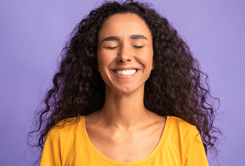 Happiness. Happy Brunette Woman Smiling With Eyes Closed, Positive Young Lady With Curly Hair Sincerely Laughing While Posing Over Purple Background In Studio, Closeup Shot With Free Space