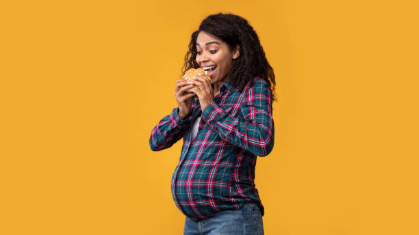 istock Pregnant African American Lady Eating Burger At Studio 1285263568