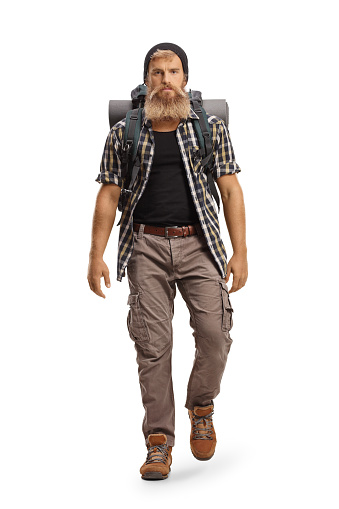 Full length portrait of a young bearded hiker with a backpack walking towards camera isolated on white background