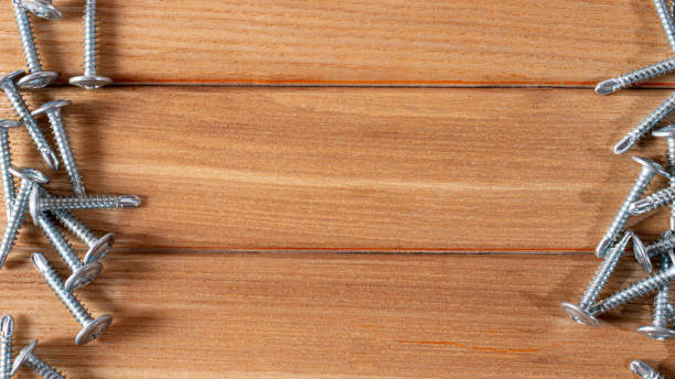 istock Self-cutters on a wood brown background banner with space for text. Construction tools, self-tapping screws for fastening. Black screw hardware. 1285264462