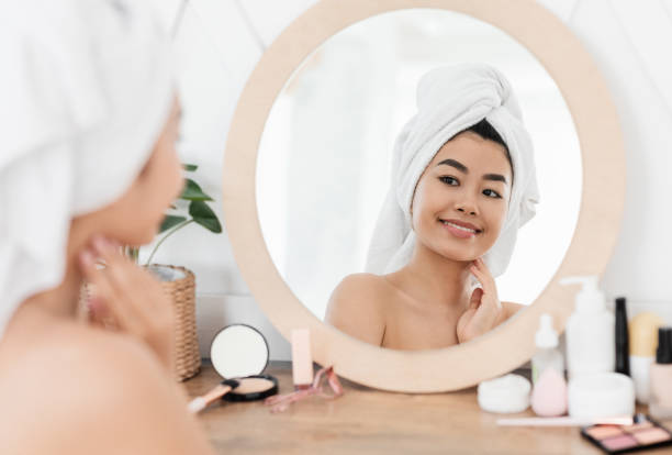 istock Smiling asian woman wrapped in towel looking at mirror 1285265111