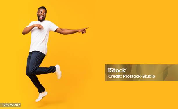 Joyful Black Guy Jumping Up And Pointing Aside Stock Photo - Download Image Now - Men, People, Jumping