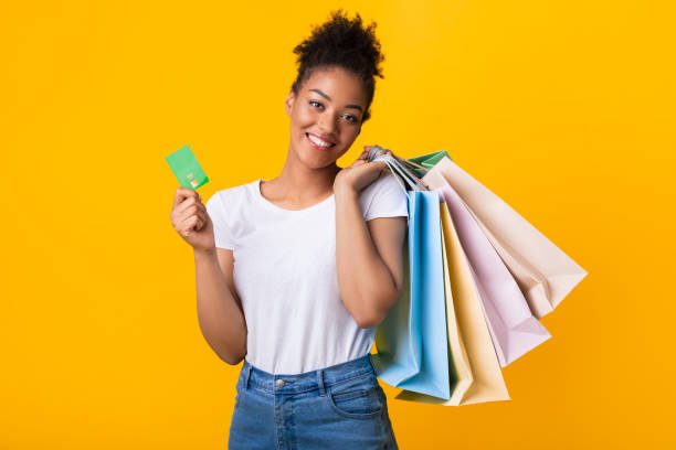 mujer negra sonriente sosteniendo tarjeta de crédito y bolsas de compras - greeting card holding women credit card fotografías e imágenes de stock