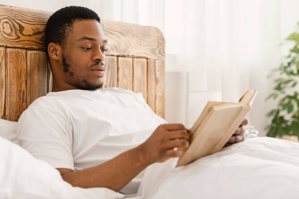 istock Black Man Enjoying Reading Book Lying In Bed At Home 1285270123