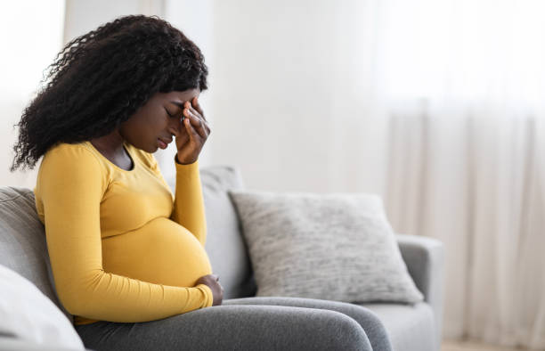 молодая беременная чернокоя жен�щина, страдающая головной болью или мигренью - human pregnancy depression sadness women стоковые фото и изображения
