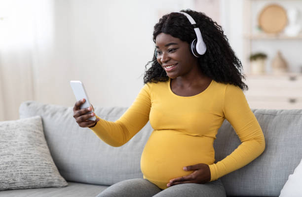istock Happy pregnant black lady with headset using smartphone 1285270477