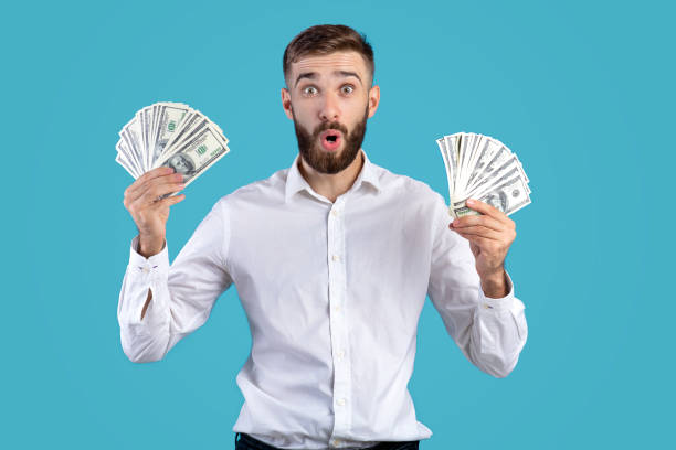 istock Shocked young man holding money banknotes on blue studio background 1285271005