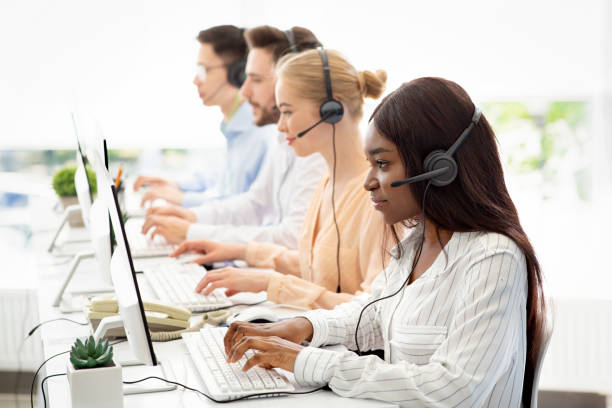 istock Focused call centre operators with headphones working with computers at open space office, blank space 1285271804