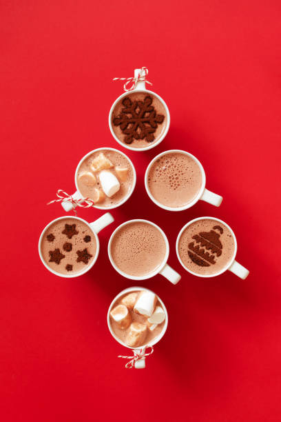 Cups with hot chocolate with marshmallows and cocoa powder decor in white mugs on red background and copy space, top view