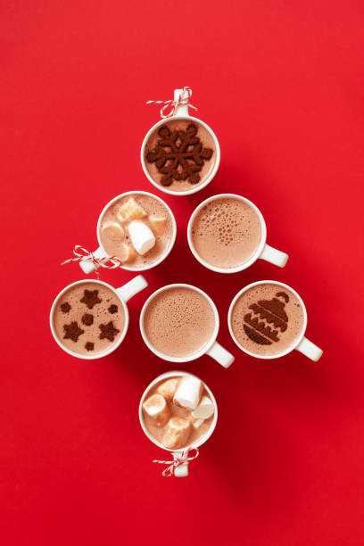 Cups with hot chocolate with marshmallows and cocoa powder decor in white mugs on red background and copy space, top view Cups with hot chocolate with marshmallows and cocoa powder decor in white mugs on red background stay Christmas tree shape, top view cappuccino photos stock pictures, royalty-free photos & images