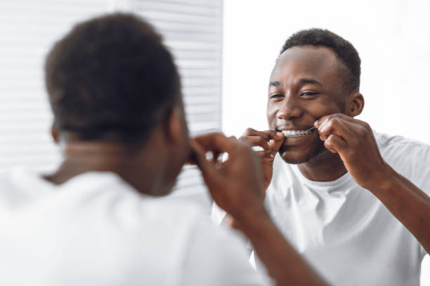 homem africano dentunte fio dental dentes usando fio dental em pé no banheiro - flos - fotografias e filmes do acervo