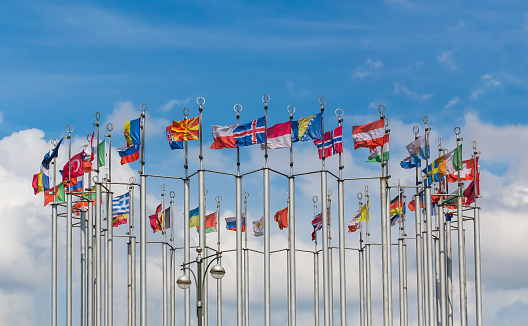 Flags of European countries on flagpoles against a blue cloudy sky