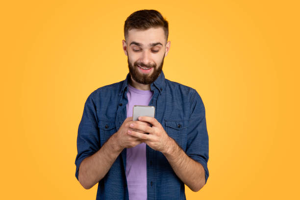 istock Handsome bearded guy with smartphone browsing internet, communicating online or shopping over orange background 1285274212