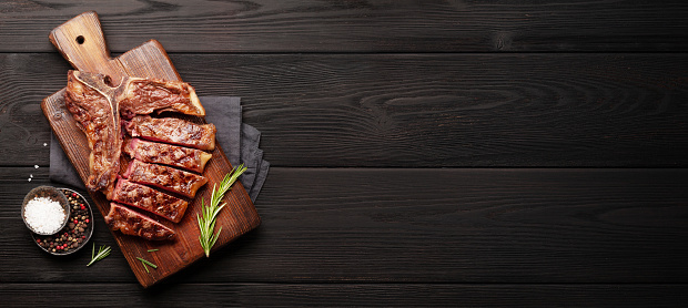 T-bone grilled beef steak with spices and herbs on wide wooden background. Top view flat lay with copy space