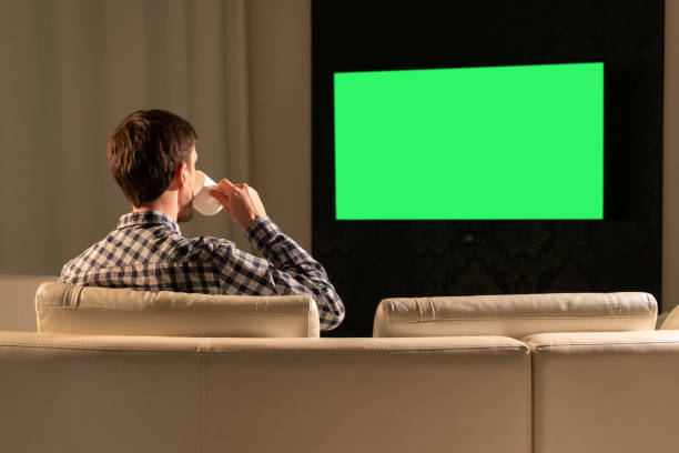 istock A man watches TV with a green screen while sitting on the couch 1285276011