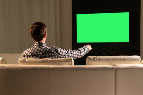 istock A man watches TV with a green screen while sitting on the couch 1285276032