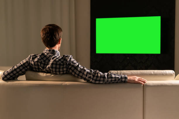 istock A man watches TV with a green screen while sitting on the couch 1285276096