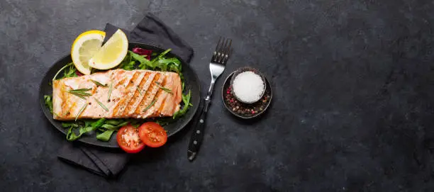 Grilled salmon fish fillet with salt, pepper and rosemary over salad leaves. On stone table. Top view flat lay with copy space