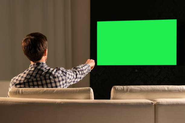 istock A man watches TV with a green screen while sitting on the couch 1285276109