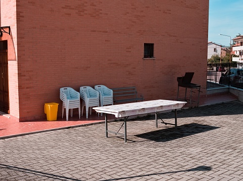An isolated table in the courtyard with stacked  chairs and a barbecue grill against the wall (Gubbio, Umbria, Italy, Europe)