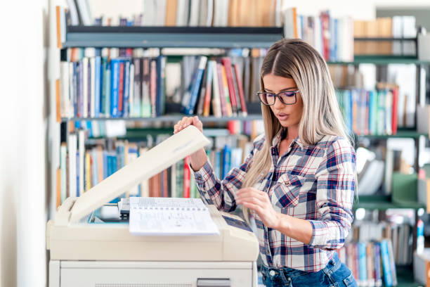 istock Lovely blonde woman smiling while using a photocopier at the library 1285284984