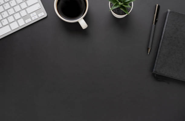 istock Top view above of Black office desk table with keyboard, notebook and coffee cup with equipment other office supplies. Business and finance concept. Workplace, Flat lay with blank copy space. 1285286881