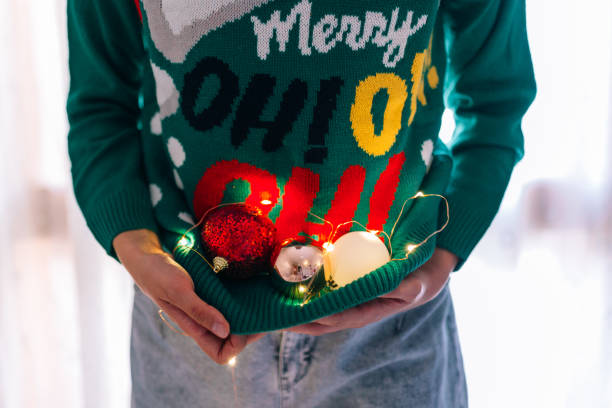 mulher irreconhecível segurando bolas de árvore de natal em um jumper de natal com luzes - ugly sweater - fotografias e filmes do acervo