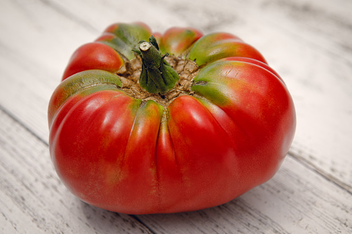 Fresh organically grown German Johnson heirloom tomato on a rustic white painted wooden background