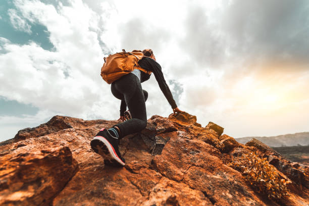 de vrouwwandelaar die van het succes op de bergpiek van de zonsopgang wandelt - de jonge vrouw met rugzak stijging aan de bergbovenland. discovery travel destination concept - klimsport stockfoto's en -beelden