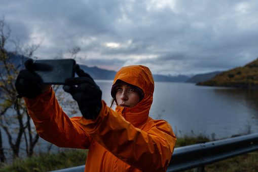 Woman hiking outdoors by a fjord in autumnal mood day: selfie time