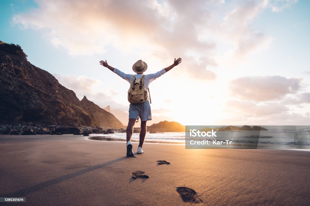 Young man arms outstretched by the sea at sunrise enjoying freedom and life, people travel wellbeing concept Travel Stock Photo