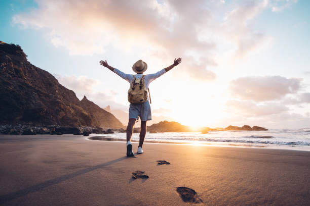 Young man arms outstretched by the sea at sunrise enjoying freedom and life, people travel wellbeing concept Young man arms outstretched by the sea at sunrise enjoying freedom and life, people travel wellbeing concept footprint photos stock pictures, royalty-free photos & images