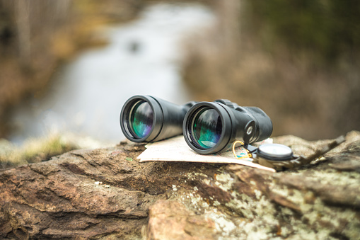 Binoculars, map and compass lie on a stone on the background of nature. Travel, tourism, outdoors concept. Navigation, GPS, orienteering