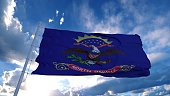North Dakota flag on a flagpole waving in the wind, blue sky background. 3d rendering