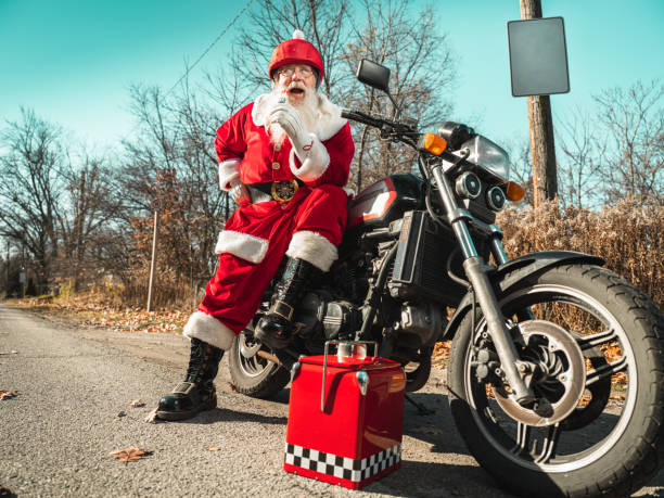 Santa Claus taking a break from riding a motor bike along the quiet residential street in suburbia. He is having a snack of cone pop-sickle.