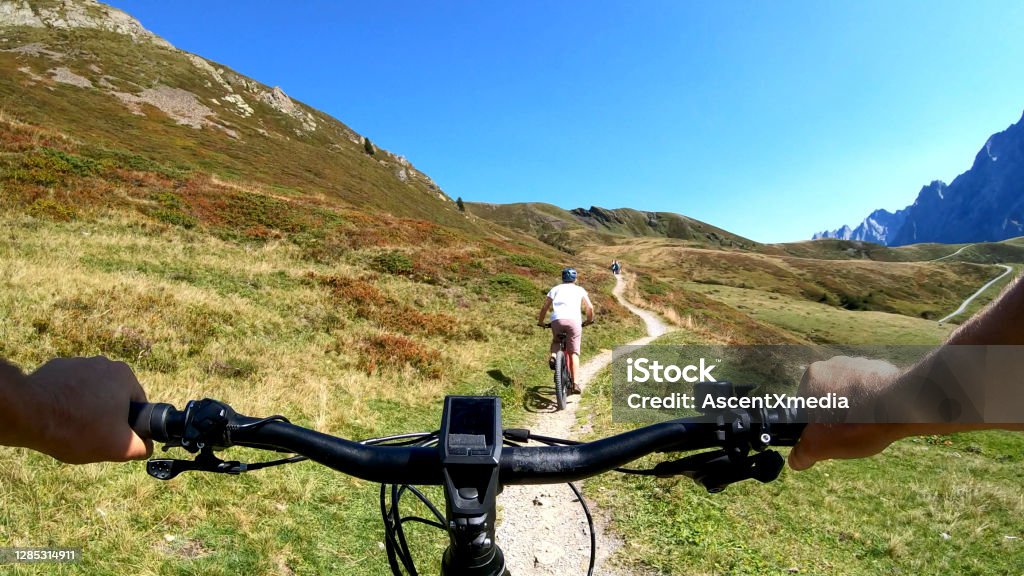 POV perspective view of e-biking along mountain slope behind a young woman mountain biking Trail and mountains in distance Electric Bicycle Stock Photo