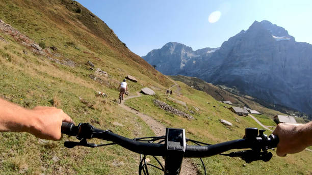 POV perspective view of e-biking along mountain slope behind a young woman mountain biking Trail and mountains in distance grindelwald photos stock pictures, royalty-free photos & images