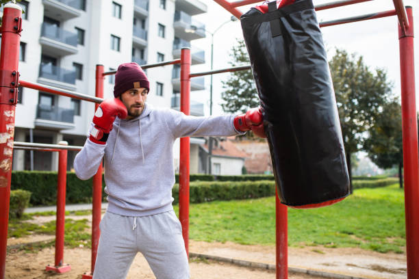 un homme attrayant poinçonnant un sac lourd à l’extérieur - men sweat combative sport boxing photos et images de collection