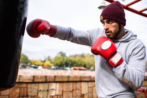 un homme jabbing un sac de poinçonnage lourd à l’extérieur - men sweat combative sport boxing photos et images de collection