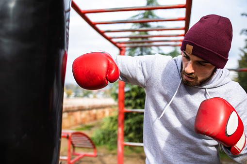 An attractive young fighter is punching a heavy bag in a street workout park on a rainy autumn day